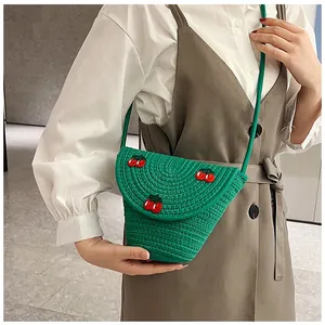 Détail d'un sac en paille tissée verte avec broderie cerise porté par un mannequin