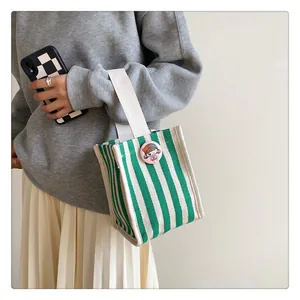 Detailed shot of a green and white striped canvas mini handbag with a cute cartoon badge