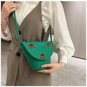 Détail d'un sac bandoulière en paille tressée verte avec broderie cerise rouge