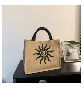 Detalle del bolso tote de yute con diseño de sol negro y asas redondas negras