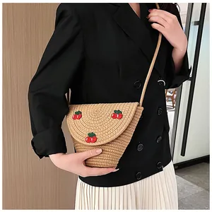 Détail d'un sac à bandoulière en paille avec broderie cerise et fermeture à rabat