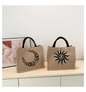 Detalle del bolso de paja tejida con asas negras y motivo de sol y luna sobre mesa