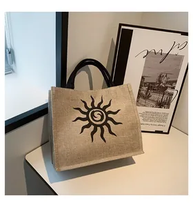 Detalle del bolso tote de yute con diseño de sol, asas negras y textura natural
