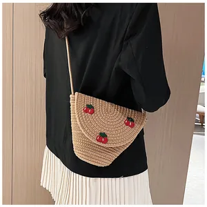 Détail du sac bandoulière en paille tressée avec broderie cerise et texture spirale