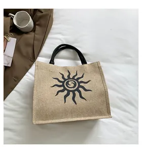 Bolso tote de lona beige con estampado de sol negro sobre fondo blanco con textura