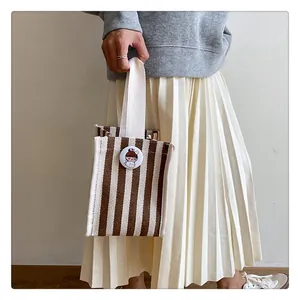 Detail of a brown striped canvas mini tote bag with badge on a casual model outfit