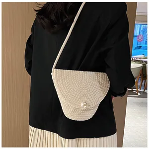 Détail du sac bandoulière tissé crème avec fermeture perle sur un mannequin en blazer