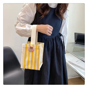 Detail of yellow and white striped canvas handbag with cute pink cartoon character brooch
