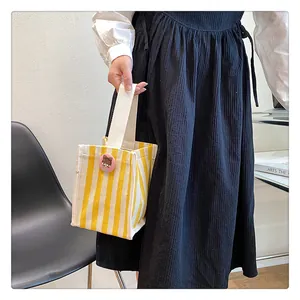 Close-up of small yellow striped canvas bag with pink badge and thick handle for daily use