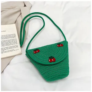 Détail du sac tressé vert avec broderie de cerises rouges sur un tissu blanc