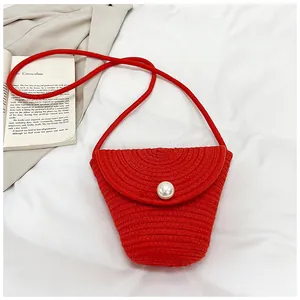 Détail du sac de plage tressé rouge avec fermoir perle sur fond en tissu blanc