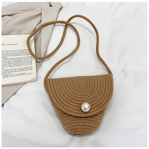 Gros plan du sac bandoulière en paille avec boucle perle sur tissu blanc doux
