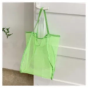 Gros plan sur un sac fourre-tout en maille vert fluo suspendu à une poignée de porte blanche