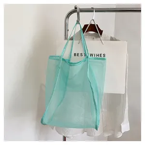 Détail du sac de plage en maille vert clair avec poignées renforcées sur un support