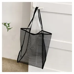 Gros plan du sac fourre-tout en maille noire suspendu à une porte en bois blanc