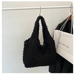 Detailed view of black pleated puffer tote bag hanging on a rack in a minimalist setting
