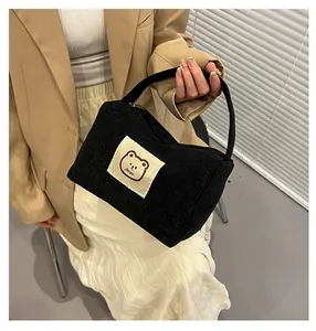 Borsa da trucco in velluto a coste con toppa a forma di orso, tenuta da una modella