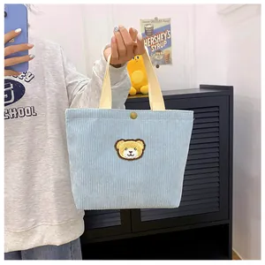 Detail van de lichtblauwe corduroy mini-handtas met schattige berenpatch en drukknoop