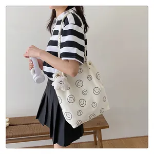 Detailed shot of white corduroy tote bag with smiley face and plush bear charm accessory