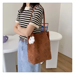 Detail view of brown corduroy tote bag with black smile prints and plush bear charm