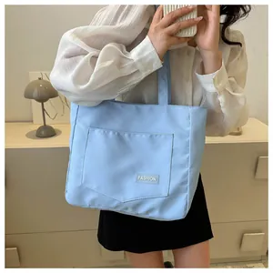Close-up of light blue canvas tote bag featuring an outer pocket and FASHION woven label