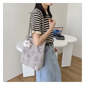 Gray corduroy tote bag with smile pattern and plush star charm worn by a model
