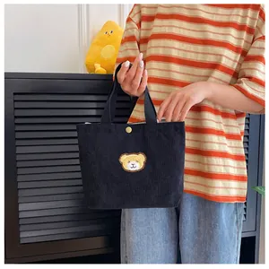 Detail van zwarte corduroy mini handtas met een schattige berenpatch en metalen drukknoop