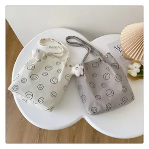 Detail of corduroy tote bags with smiley prints and plush bear charms on a white table