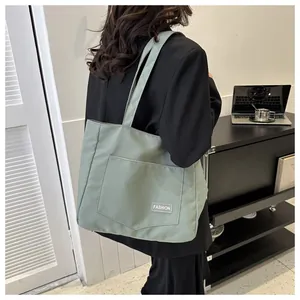 Close-up of sage green canvas tote bag with fashion label and large front pocket