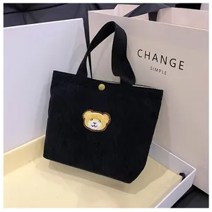 Detail van zwarte corduroy mini handtas met beertje borduursel en gouden metalen drukknoop