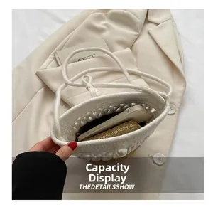 Detail showing capacity of cream woven bucket bag with pearl accent on a beige blazer