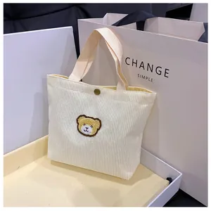 Detail van crème corduroy mini-tas met schattige berenpatch en metalen drukknoop