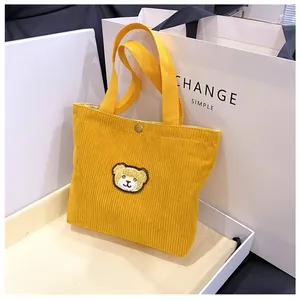 Detail van gele corduroy mini-tote met berenborduursel en een metalen drukknoop
