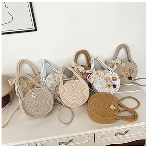 Détail de sacs ronds tissés avec décor floral et bandoulière sur un meuble blanc