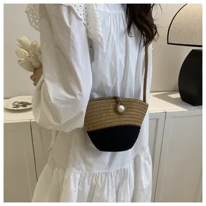 Detail of hand-woven straw bucket bag with brown-black contrast and pearl buckle