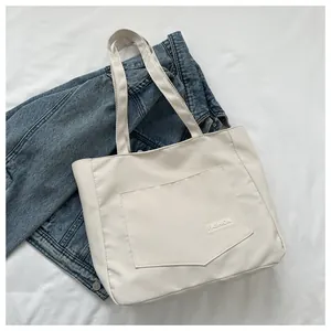 Detailed close-up of cream canvas tote bag with front pocket and fashion label on fabric