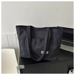 Close-up of black canvas tote bag with large front pocket and white fashion label