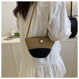 Detail of a two-tone woven crossbody bag with pearl accent and slim strap on model