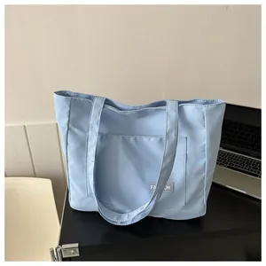 Detail of light blue canvas tote bag featuring front pocket and minimalist fashion label
