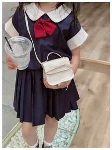 Girl's mini cream crossbody bag with bow detail paired with navy blue school style dress
