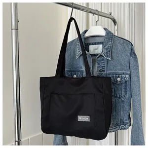 Detail of black nylon tote bag with front pocket and fashion label on denim background