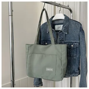 Detail of sage green canvas tote bag showing large front pocket and FASHION label