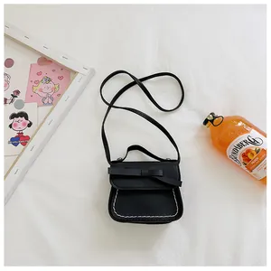 Detail of girls mini black leather crossbody bag featuring a bow and white stitching