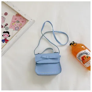 Detail view of light blue girls bow crossbody bag with white stitching and top handle