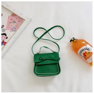 Detail of green mini crossbody bag with bow decoration and contrast stitching on white cloth