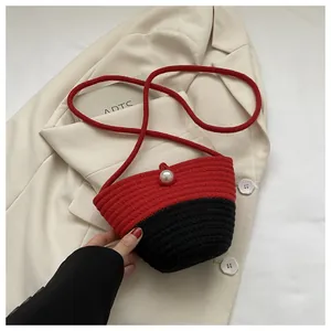Detail of red and black woven crossbody bag with white pearl closure and thin strap