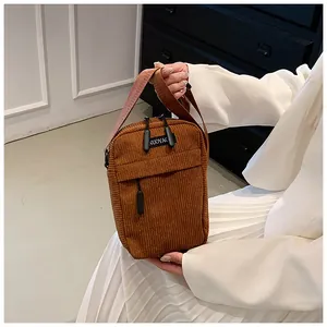 Detail of a brown corduroy crossbody bag featuring a front zipper and woven brand label