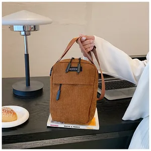 Close-up of brown corduroy crossbody bag with dual zippers and woven handle details
