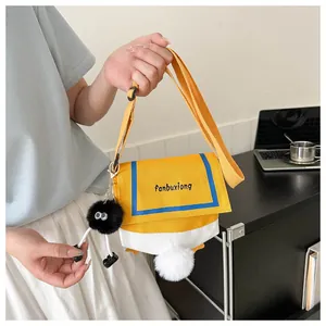 Detail of yellow canvas crossbody bag featuring embroidery and fluffy plush charms
