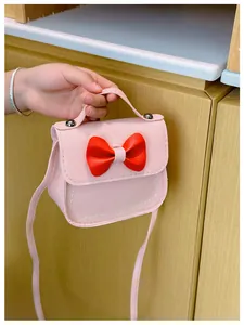 Vue détaillée du mini sac bandoulière rose pour enfant avec nœud rouge et fermoir argent